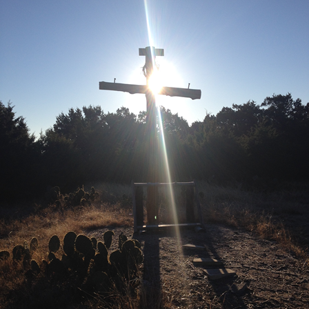 Wooden cross in an open field on the northwest side of Austin, Texas. Sunrise projects in a solid ray.