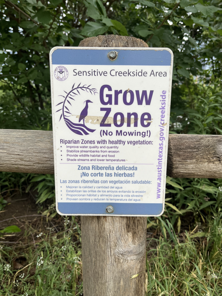 Photograph taken in Austin, Texas at the Town Lake Trail. Features a sign marker that reads: "Grow Zone (No Mowing!) to protect the riparian zone and its healthy vegetation in support of the surrounding ecosystem.