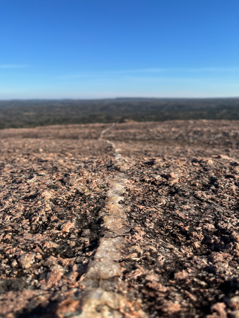 Photo taken at Enchanted Rock. Tiny but distinct quartz path emerging in the limestone, leading into the deep blue horizon.